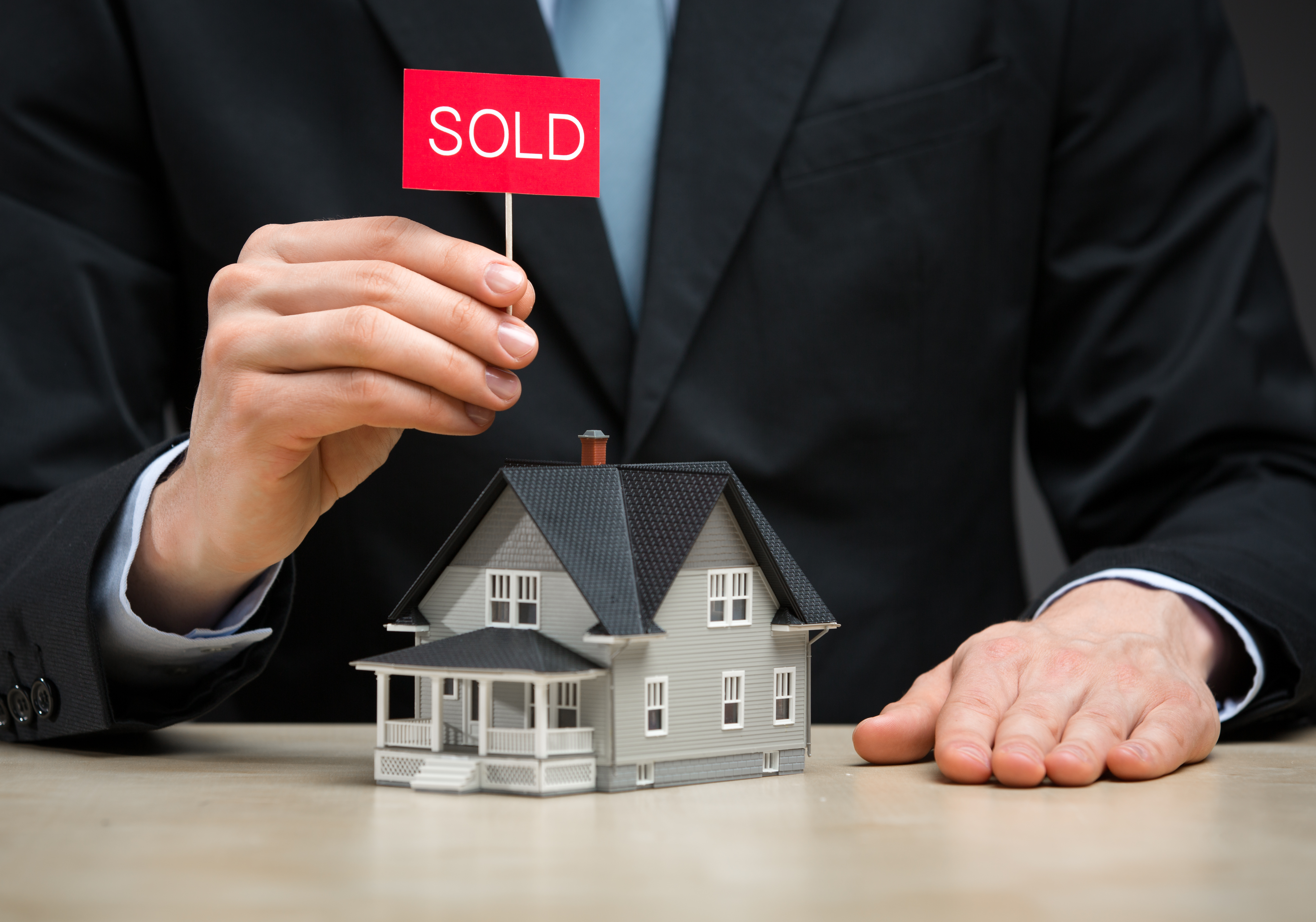 Image of a person holding a sold sign over a model house - represents that A Property Millionaire knows how to secure the best property deals